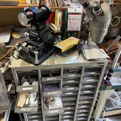 大量の電工作部品、オシロスコープ、デジタルマルチメーターなどの計測機器、抵抗器、トランジスタ、コンデンサの画像