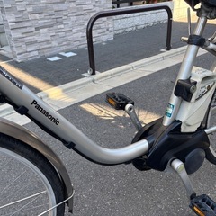 Panasonic製のシルバー電動アシスト自転車、バスケットと前照灯付き。の画像