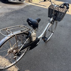 Panasonic製のシルバー電動アシスト自転車、バスケットと前照灯付き。の画像