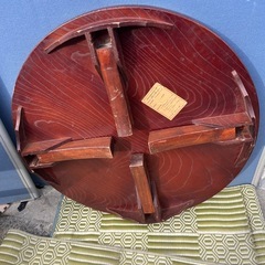 円形の木製座卓、折りたたみ可能でダークブラウンの仕上げ。の画像