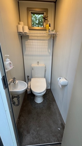 洋式トイレと小型洗面台が備わったプレハブ式トイレ、収納棚付きで便利。