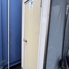 洋式トイレと小型洗面台が備わったプレハブ式トイレ、収納棚付きで便利。の画像